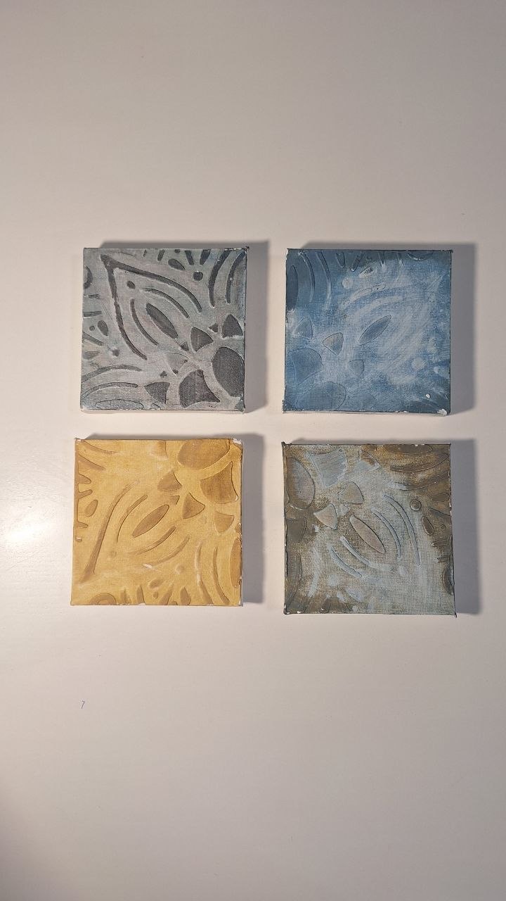 Four small square textured artworks in muted blue, yellow and metallic tones